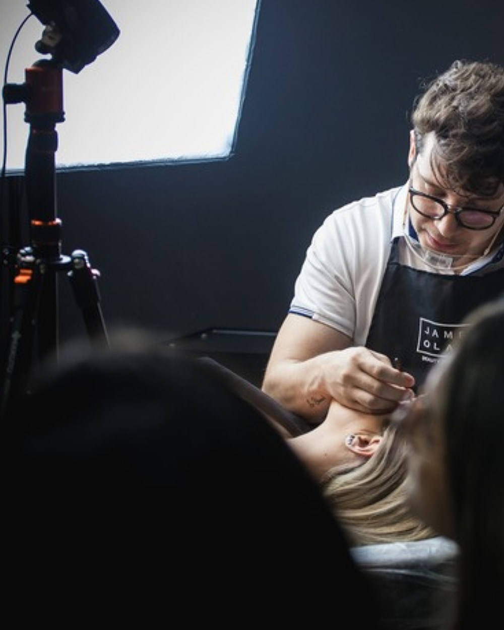 James Olaya executando um procedimento sob a luz de estúdio, com a turma acompanhando em primeiro plano
