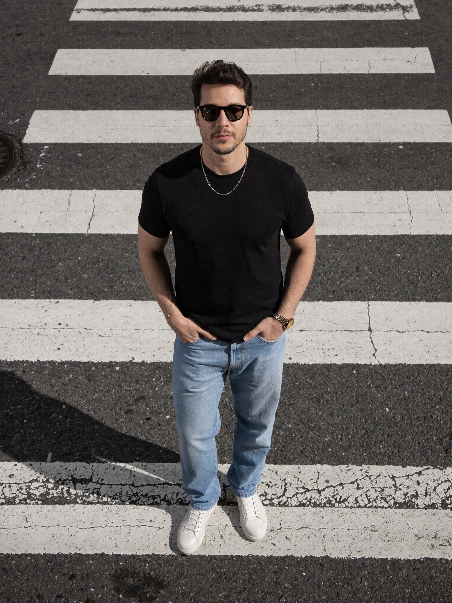 James Olaya de camiseta preta e jeans, em pé numa faixa de pedestre, visto de cima